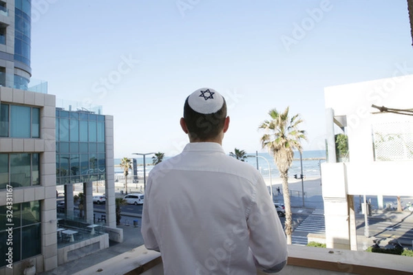 Fototapeta young Jew stands next to beautiful buildings in the city and looks at the street and the seashore