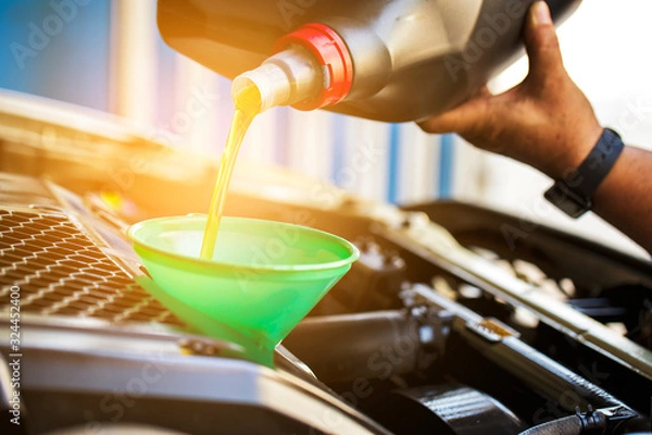 Fototapeta Car mechanic replacing and pouring fresh oil into engine..