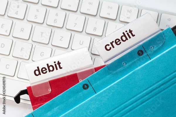 Fototapeta tow hanging folders on in red and in blue on a keyboard having tabs with the words debit and credit on it