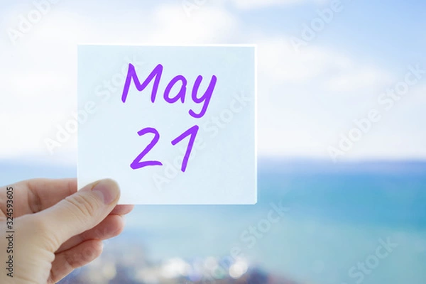 Fototapeta May 21st. Hand holding sticker with text May 21 on the blurred background of the sea and sky. Copy space for text. Month in calendar concept