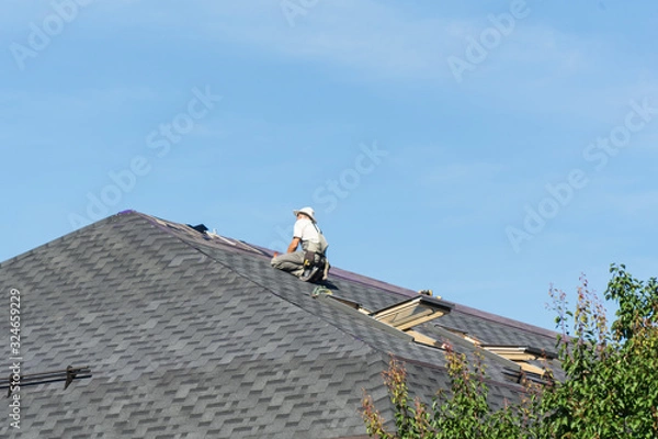 Fototapeta The man on the roof. Photo of a worker repairing the roof of the house.