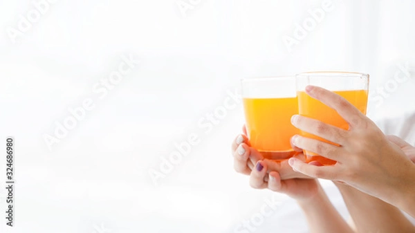 Fototapeta Close up women's hand hold glass of orange juice on bright background with copy space on left side.