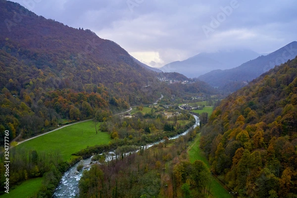 Fototapeta Alpine valley with mountain river and village cantoira with a lot of green  grass in a foggy autumn day 