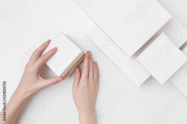Fototapeta Mock up of white present box in women's hands on the white background surrounded with many different size white boxes