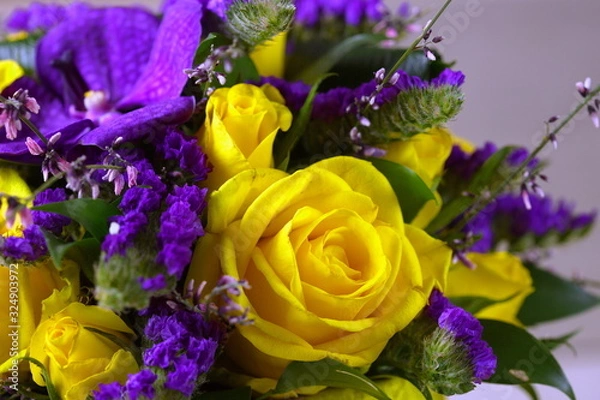 Fototapeta Close-up of a beautiful spring bouquet with yellow roses and purple orchids. Decorative composition of a greeting card for a birthday holiday. Copy space.