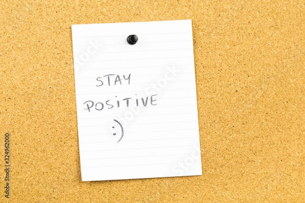 Fototapeta Stay positive text on white notebook paper sheet hanging on cork card board. Motivating business background