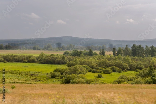 Fototapeta Calm blue sky in the early autumn sky over green fields, trees, forests and huge mountains. A lot of meadow herbs around. Day. Travel through nature landscape