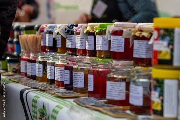 Fototapeta Beervelde/Belgium - October 13 2019: A bunch of freshly made pots of jam. The jars are colorful due to the homegrown fruit. The glass pots are stacked in rows and displayed at a local market.
