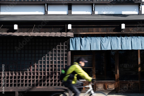 Obraz blur of a man ride bicycle ,wooden wall of window and old house in Japan. low key and soft focus.