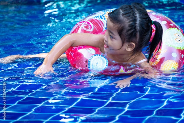 Obraz Portrait of cute little asian girl having fun in swimming pool, floating in blue refreshing water with colurful rubber ring
