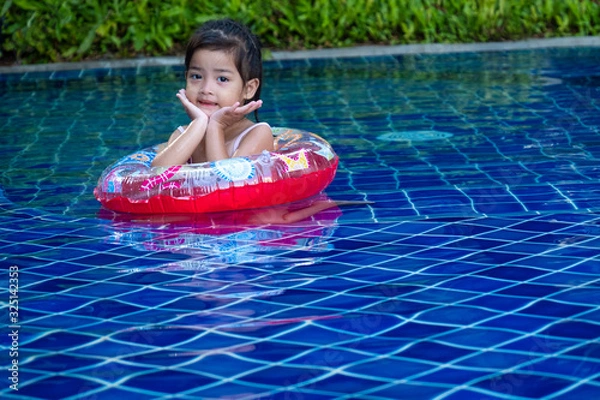 Obraz Portrait of cute little asian girl having fun and smiling in the swimming pool, floating in blue refreshing water with colurful rubber ring