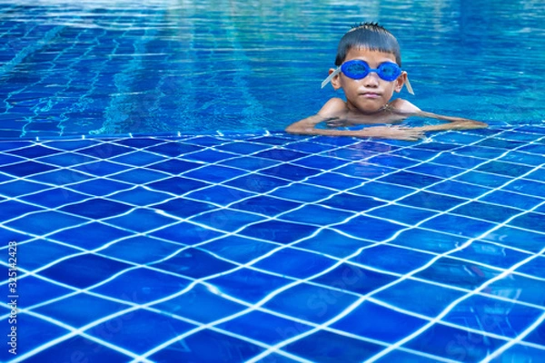 Obraz Portrait of asian boy ware a blue glasses and floating at the corner of swimming pool and blue refreshing water