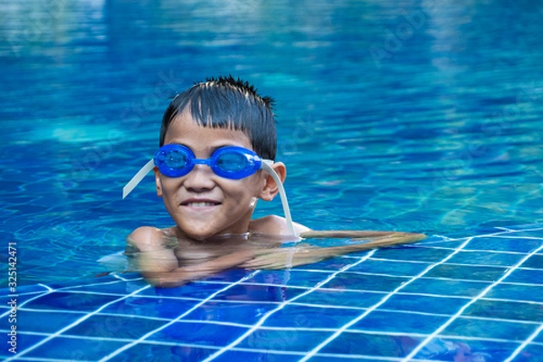 Obraz Portrait of asian boy ware a blue glasses and floating at the corner of swimming pool and blue refreshing water