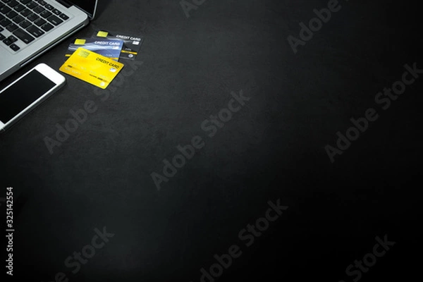 Obraz Laptop, white mobile phone and credit cards against empty dark background