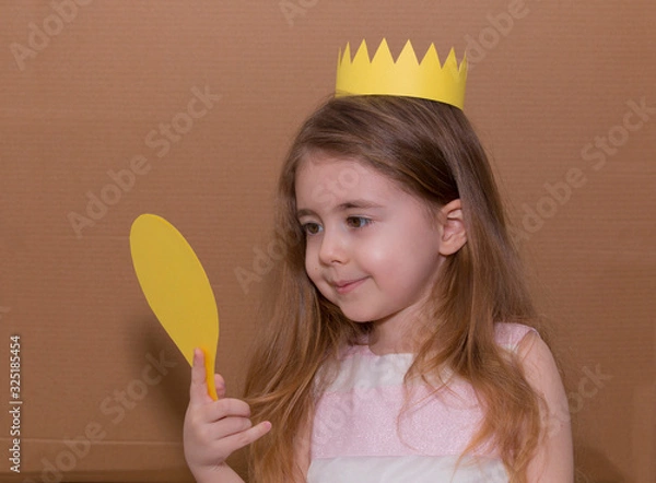 Obraz Portrait of emotional little girl with crown a yellow paper holding a mirror. handmade. cardboard background