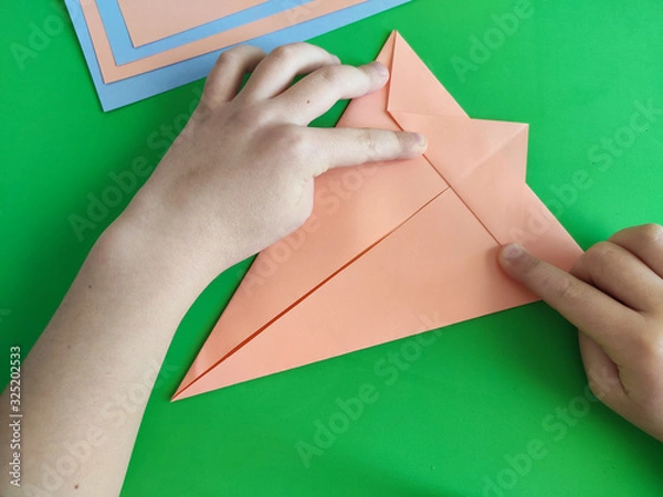 Fototapeta Origami step by step. How to make a paper bunny for Easter greetings and fun. DIY concept. Top view of kids hands making papercraft. Step by step photo instruction 4 out of 11.