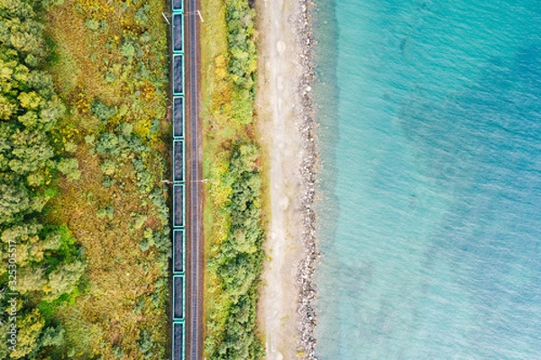 Fototapeta Lake Baikal shore with green forest trees and turquoise water, aerial top down view. Freight train with coal on railroad of Trans-Siberian Railway. East Siberian Railway in Buryatia, Siberia, Russia