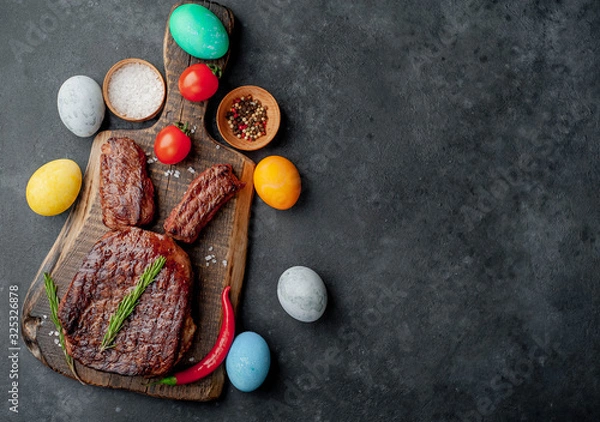 Fototapeta Grilled festive Easter steak with spices and colorful eggs. Easter bunny on stone background with copy space for your text.