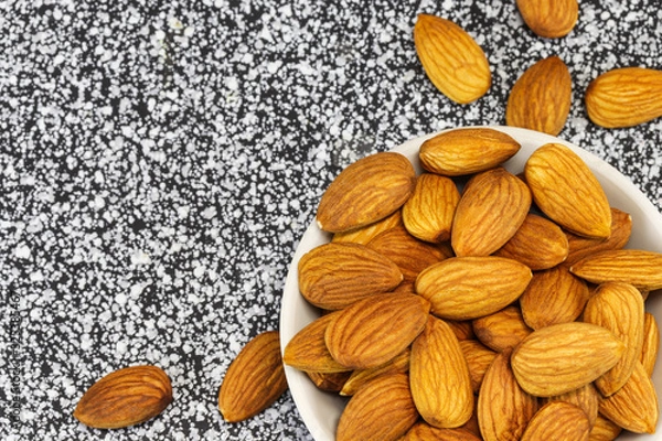 Obraz Almond nuts lie in a white glass bowl and on gray-white marble