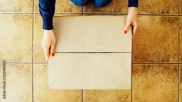 Fototapeta Woman hands opening a parcel contains a gift. Unpacking box with another box. Surprise. Craft present box. People, delivery, shipping service, opening cardboard box or parcel at home.