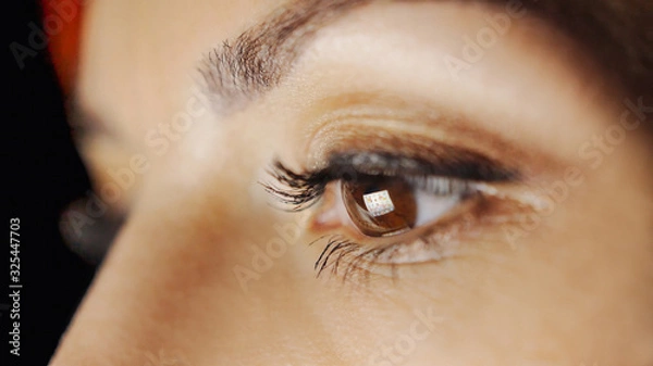 Fototapeta Close-up of young woman eyes looking at monitor, working from home remotely with computer, laptop. Screen light reflected in eyes. Evening woman freelancer working, reading books, watch video online.