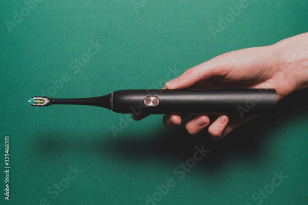 Fototapeta Top view of a hand that holds a black electric toothbrush on a green background