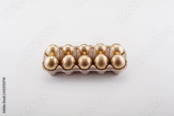 Fototapeta A dozen Golden eggs in a cassette top view, on a white background. The concept of Easter, abundance and preservation of Finance.
