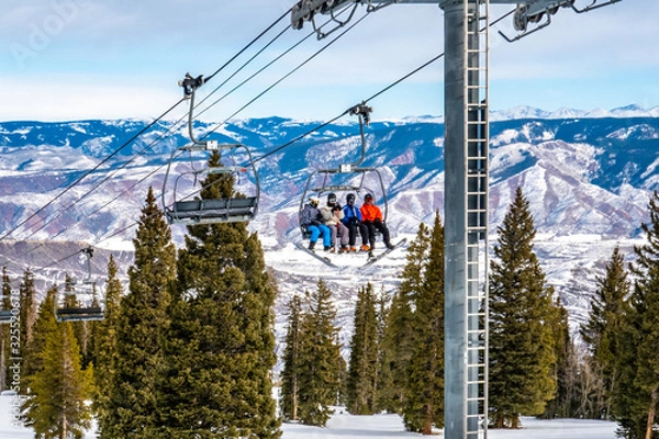 Fototapeta Skiers and snowboarders ascend the Alpine Springs chairlift at the Aspen Snowmass ski resort, in the Rocky Mountains of Colorado on a partly cloudy winter day. 
