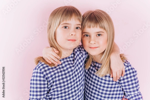 Fototapeta Happy adorable twin blodnie caucasian girls together having fun, hugging and playing. Smilling happy kids. Childhood, twins, friendship concept 