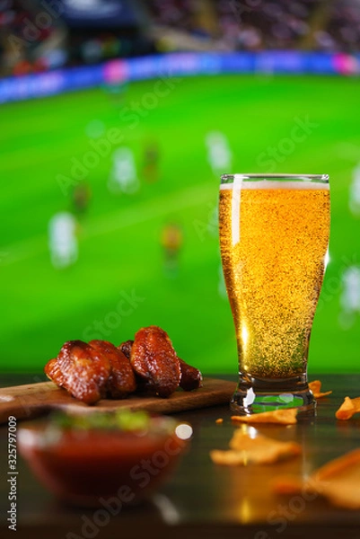 Fototapeta Spicy barbecue chicken wings, tomato salsa, nachos and beer on dark wooden bar table. Football on background, high resolution