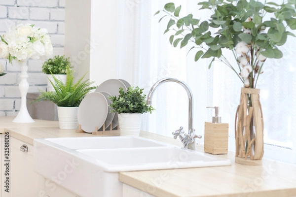 Obraz kitchen area with artificial flowers in flower pots, plates on a wooden stand, a large sink with a tap..