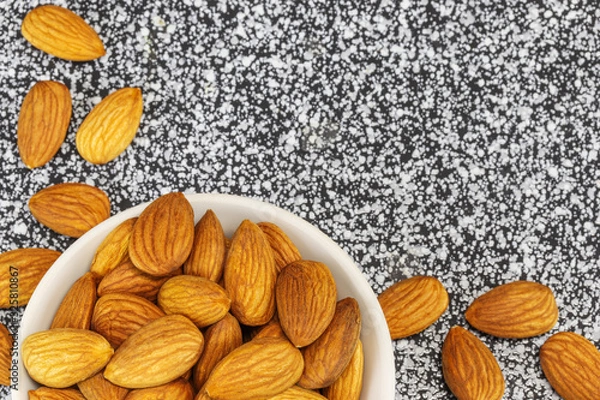 Obraz Almond nuts in a white bowl and on a black-white marble surface