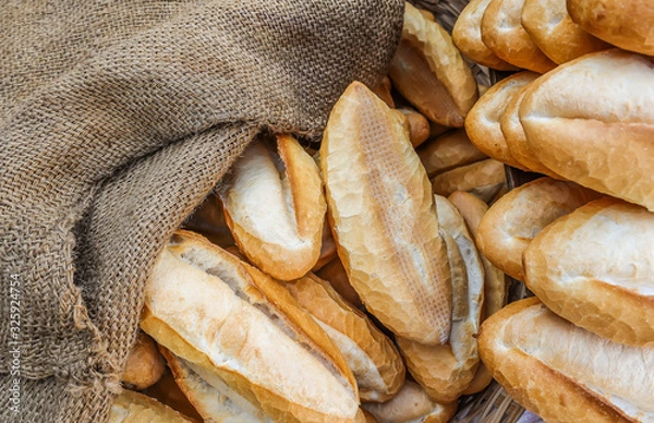 Obraz Loaves of a freshly baked baguette for sale, covered with sackcloth. Close-up view from the top. 
