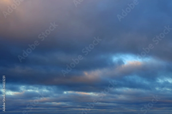 Fototapeta Low cloud cover. Dense dark clouds lit by the sun with gleams of the blue sky as expressive dramatic backdrop.