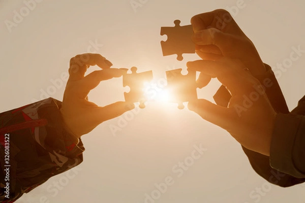 Fototapeta Three pieces of puzzles in the hands of a group of people on the background of the glare of the sun. The concept of teamwork, interaction.