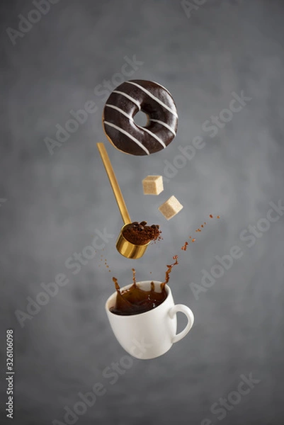 Fototapeta a cup of coffee with a splash freezes in the air a coffee spoon hovering in the air pours out coffee falling pieces of sugar overhang a white striped chocolate donut