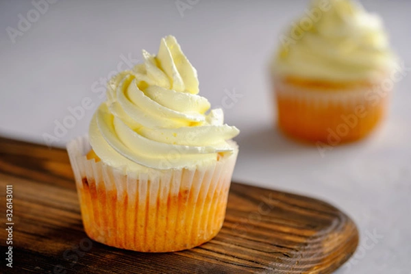 Fototapeta Delicate and delicious lemon cupcakes with cream on a wooden board