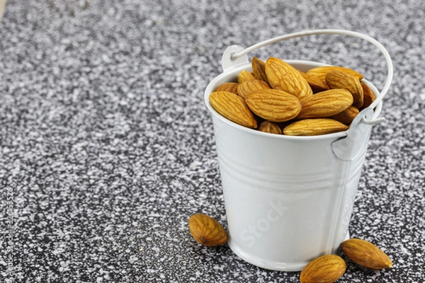 Obraz A white metal bucket filled with almond nuts stands on black and white marble