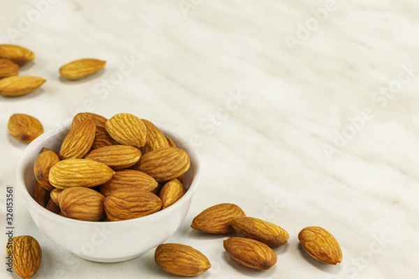 Obraz Almond nuts lie in a white bowl and on a white marble surface