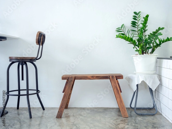 Fototapeta White cafe decoration minimal style. Green leaves in white pot and wooden bench on white wall background.