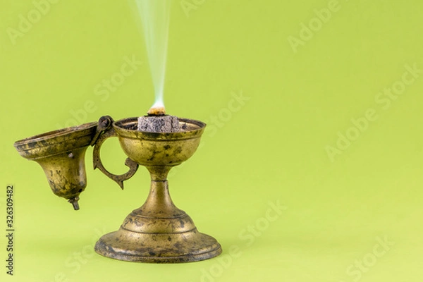 Fototapeta Old frankincense burner with burning frankincense on hot coal. Isolated on color background, copy space for text. Traditional method for incense burning.