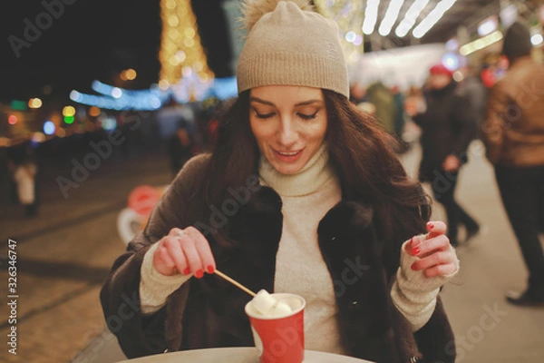 Fototapeta woman drinks cocoa with marshmallows on the street