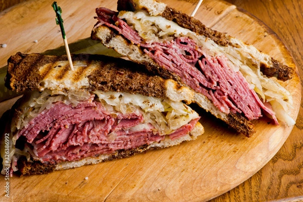 Fototapeta Reuben Sandwich, classic traditional American bar/pub menu item, on grilled rye bread, corned beef, Swiss cheese, sauerkraut and topped with thousand island dressing and french fries in background.