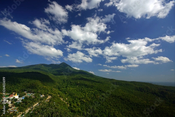 Fototapeta Beautiful view of bright green hills and blue sky with clouds. Black hadows of clound on hill. Small village with temple
