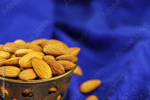 Obraz A metal bowl filled with almonds on a blue background
