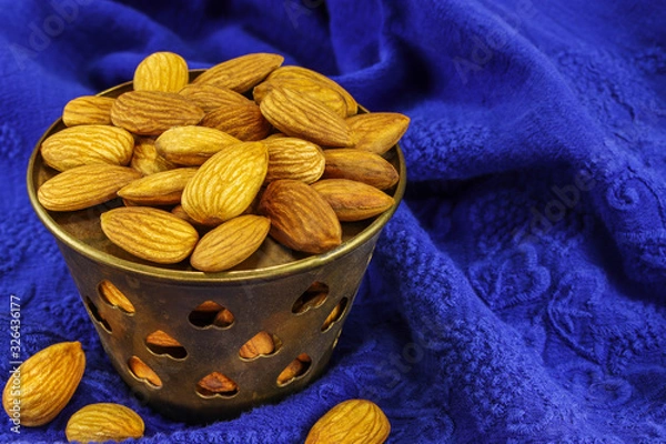 Obraz A metal bowl filled with almonds stands on a blue material with a pattern
