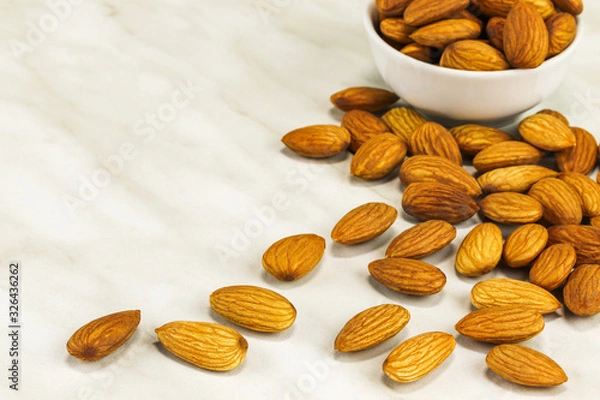 Obraz Almonds lie on a white marble surface and in a white bowl