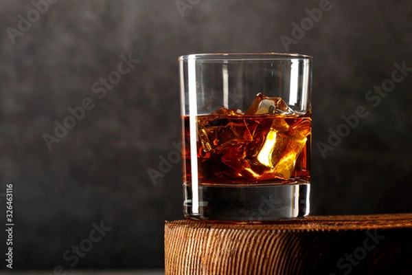 Fototapeta Whiskey with ice or brandy in a glass on a rustic background. Whiskey with ice in a glass. Whiskey or brandy. Selective focus.