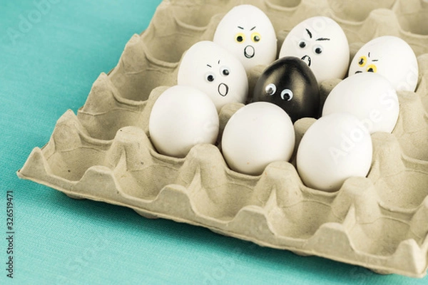 Fototapeta Black egg among angry, prejudiced white eggs attacking the black one. Xenophobic, racist concept.