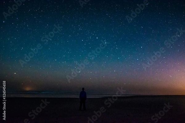 Fototapeta Adventurous man watching the stars on a beach at night. 